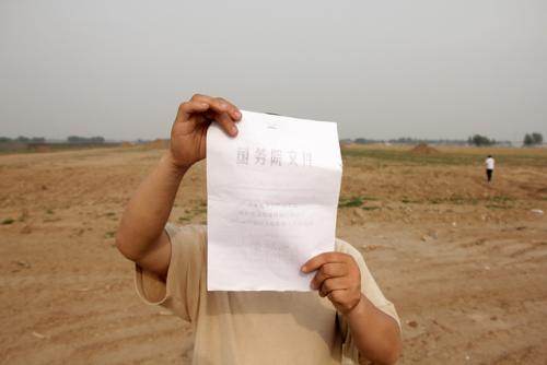 Ce paysan cache son visage devant la photocopie d'un texte du "Conseil d'Etat" censé protéger les terres cultivables.