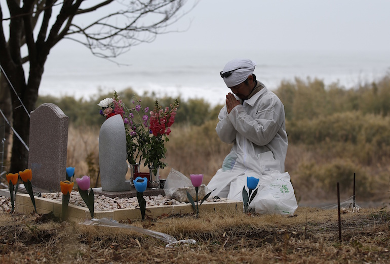 Un réfugié nucléaire prie devant la tombe de sa famille morte durant le tsunami.