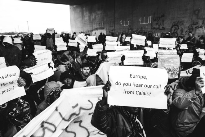 Assis, les manifestants brandissent leurs pancartes face aux forces de l’ordre. « Europe, entends-tu notre appel de Calais ? ». © Marie Magnin