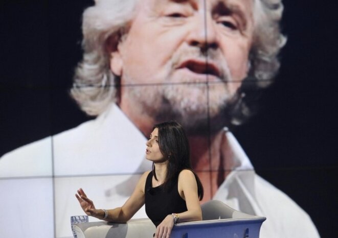 Virginia Raggi lors d'une émission de télévision, avec Beppe Grillo en fond d'écran derrière elle © Capture d'écran L'unita.tv Virginia Raggi lors d'une émission de télévision, avec Beppe Grillo en fond d'écran derrière elle © Capture d'écran L'unita.tv