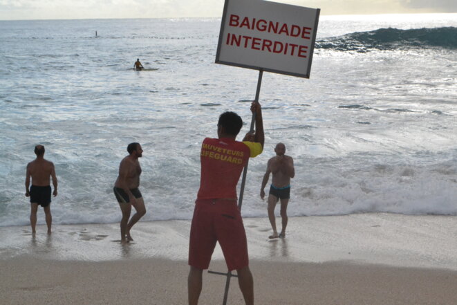 A lifeguard holds a sign announcing "Bathing forbidden". Only secured beaches are officially open to bathers on La Réunion's west coast. © Julien Sartre A lifeguard holds a sign announcing "Bathing forbidden". Only secured beaches are officially open to bathers on La Réunion's west coast. © Julien Sartre