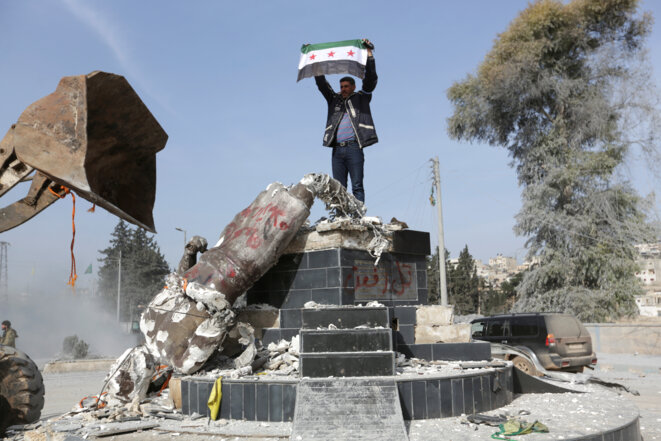 Le 18 mars 2018 à Afrin, un homme brandit son drapeau en lieu et place de la statue déboulonnée © Reuters/Khalil Ashawi