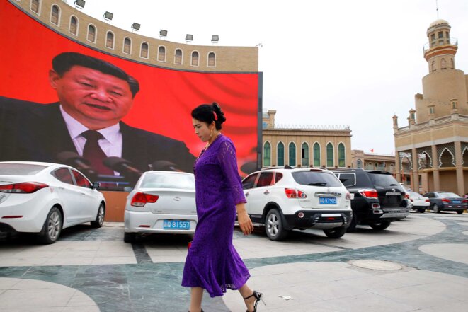 Une femme ouïgoure passe devant un écran géant qui diffuse des messages du Parti communiste et des images du président Xi Jinping sur la place principale de Kashgar. © Reuters/Thomas Peter Une femme ouïgoure passe devant un écran géant qui diffuse des messages du Parti communiste et des images du président Xi Jinping sur la place principale de Kashgar. © Reuters/Thomas Peter