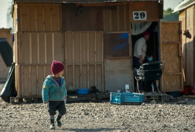 Un enfant devant une cabine en bois, au camp de migrants et de réfugiés de Grande-Synthe, dans le Nord de la France, le 4 octobre, 2016. • Crédits : Philippe Huguen - AFP Un enfant devant une cabine en bois, au camp de migrants et de réfugiés de Grande-Synthe, dans le Nord de la France, le 4 octobre, 2016. • Crédits : Philippe Huguen - AFP