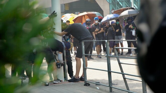 Les manifestants tentent de faire un "parapluie bloc" pendant qu'un des leurs coupe à la disqueuse un lampadaire équipé de caméra. Hong Kong le 24/08/2019. © Pierre Thomas Les manifestants tentent de faire un "parapluie bloc" pendant qu'un des leurs coupe à la disqueuse un lampadaire équipé de caméra. Hong Kong le 24/08/2019. © Pierre Thomas