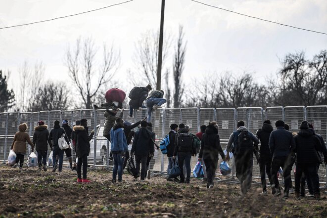 Des migrant·e·s sautent des barrières érigées par l'armée turque près du point de passage de Pazarkule, le 4 mars 2020 (Ozan Kozé/AFP).