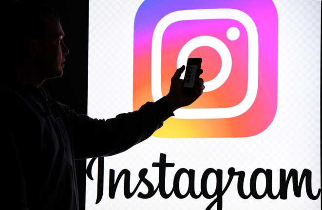 Un homme tient son smartphone devant le logo Instagram. © AFP