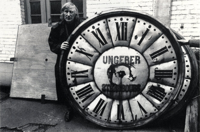 Anonyme, Tomi Ungerer avec un cadran d’horloge monumentale de la firme Ungerer, Vers 1990-1993 Photographie Archives du Musée Tomi Ungerer – Centre international de l’Illustration, Strasbourg © Musées de la Ville de Strasbourg Anonyme, Tomi Ungerer avec un cadran d’horloge monumentale de la firme Ungerer, Vers 1990-1993 Photographie Archives du Musée Tomi Ungerer – Centre international de l’Illustration, Strasbourg © Musées de la Ville de Strasbourg