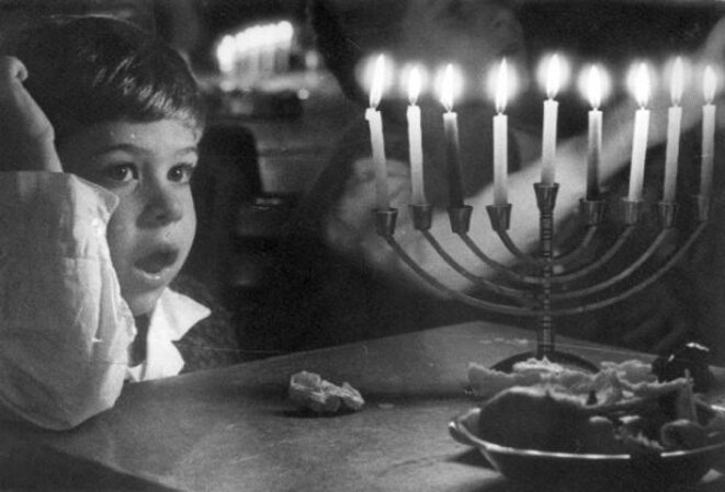 Un enfant devant une hanoukkia brillant de tous ses feux à Zot Hanoucca (8e jour). © Domaine Public Un enfant devant une hanoukkia brillant de tous ses feux à Zot Hanoucca (8e jour). © Domaine Public