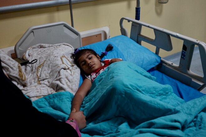 Ilaf, 5 ans, née polydactyle et sans anus, tient la main de sa mère dans son lit d'hôpital (Bassorah, avril 2021) © Rachida El Azzouzi