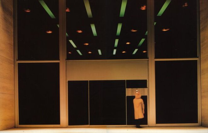 L'architecture gigantesque et froide de l'imposante façade de l'immeuble contre laquelle se cogne la solitude de Lotte, déréalise l'ensemble. Aux lignes droites acérées et dures du métal et du bois brut, répond, ironiquement, la fausse perspective en biais de lueurs au néon vert qui accentuent un peu plus l'hostilité d'un environnement devenu impersonnel. Photo: X - tous droits réservés. L'architecture gigantesque et froide de l'imposante façade de l'immeuble contre laquelle se cogne la solitude de Lotte, déréalise l'ensemble. Aux lignes droites acérées et dures du métal et du bois brut, répond, ironiquement, la fausse perspective en biais de lueurs au néon vert qui accentuent un peu plus l'hostilité d'un environnement devenu impersonnel. Photo: X - tous droits réservés.