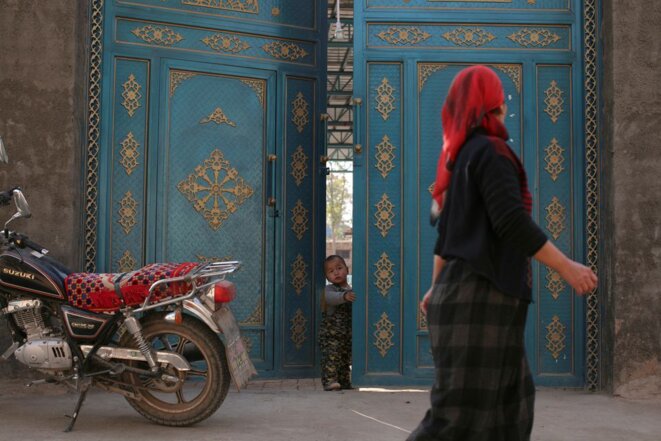 Un enfant regarde par une porte alors qu'une femme ouïghoure passe dans un quartier résidentiel de Turpan, dans la région autonome ouïghoure du Xinjiang, le 31 octobre 2013. REUTERS/Michael Martina/File Photo Un enfant regarde par une porte alors qu'une femme ouïghoure passe dans un quartier résidentiel de Turpan, dans la région autonome ouïghoure du Xinjiang, le 31 octobre 2013. REUTERS/Michael Martina/File Photo