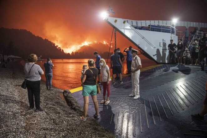 Des personnes montent à bord d'un ferry afin d'être évacuées alors qu'un incendie de forêt s'approche du village de Limni, en Grèce. 6 août 2021. © STR / NurPhoto / NurPhoto via AFP
