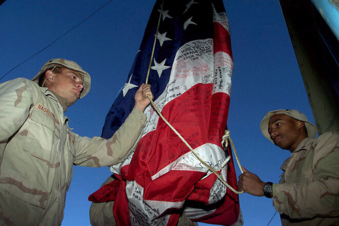 Aéroport de Kandahar, Afghanistan, le 18 décembre 2001. Deux marines américains hissent un drapeau signé par des proches des victimes du 11 septembre 2001. © Photo de Rick Loomis / LA Times / AFP Aéroport de Kandahar, Afghanistan, le 18 décembre 2001. Deux marines américains hissent un drapeau signé par des proches des victimes du 11 septembre 2001. © Photo de Rick Loomis / LA Times / AFP