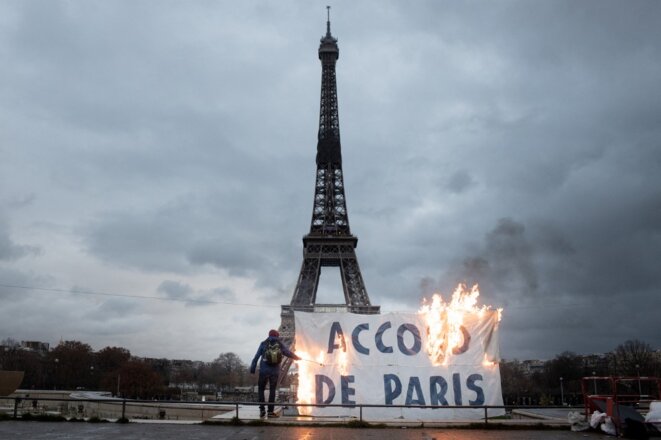 Des militants d'Extinction Rebellion brûlent une banderole, le 12 décembre 2020, sur laquelle est inscrit “Accord de Paris” pour dénoncer l'inaction climatique du gouvernement français, cinq ans jour pour jour après la signature du texte. © Frédéric Migeon / Hans Lucas / Hans Lucas via AFP