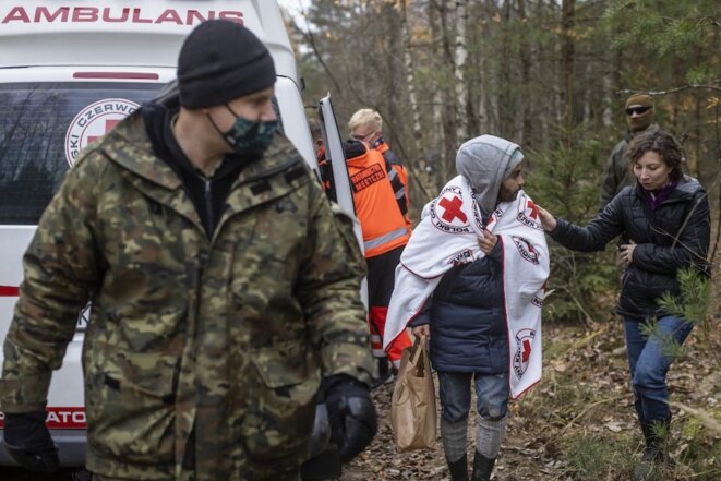 Epuisé, un jeune libanais de 24 ans marche couvert d’une couverture de la Croix-Rouge polonaise et escorté par la police des frontières. La députée polonaise Daria Gosek-Popiolek tente de le réconforter. © Wojtek Radwanski / AFP