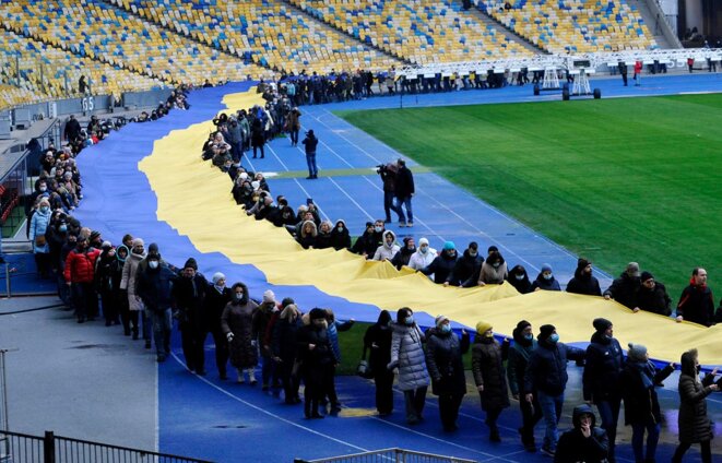 Un drapeau national ukrainien géant est déployé dans un stade pour marquer la "Journée de l'unité" à Kiev, le 16 février 2022. © Photo Sergei Chuzavkov / AFP